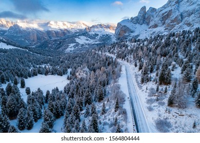 Aerial view of Curved road in the snowy mountains of Italian Alps in South Tyrol with dolomites in background / Sunny winter day with harsh shadows and lot of snow