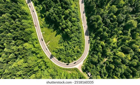 Aerial view of a curving road through a forest. A winding road cuts through a lush green forest, as seen from above. Road in the serpentine mountains. Traffic of cars through the split forest on the - Powered by Shutterstock