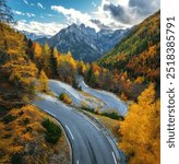 Aerial view of curvy mountain road and orange forest in golden autumn in Slovenia. Top view of winding road, colorful trees, sky, rocks  in fall. Empty road through the woods. Landscape with roadway