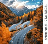 Aerial view of curvy mountain road and orange forest in golden autumn in Slovenia. Top view of winding road, colorful red trees, sky, rocks  in fall. Empty road in woods. Landscape with roadway