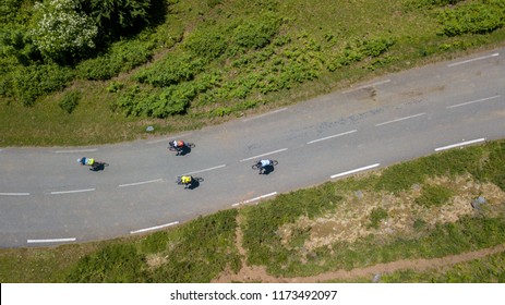 Aerial View Of Cyclists Riding Along A Road Between Green Meadows.