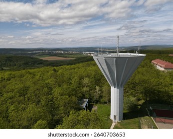 An aerial view of a cylindrical water tower surrounded by a lush green landscape of tall trees