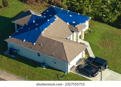 Aerial view of damaged in hurricane Ian house roof covered with blue protective tarp against rain water leaking until replacement of asphalt shingles - Shutterstock ID 2327555715