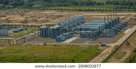 Aerial view of data center cooling infrastructure with cooling towers, water storage tanks, industrial piping systems, and utility buildings within a high-tech industrial complex under construction.