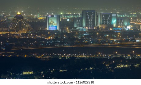 Aerial View To Deira District With Airport On Background Timelapse And Illuminated Buildings. Top View From Dubai Downtown. Traffic On The Road. Dubai, UAE