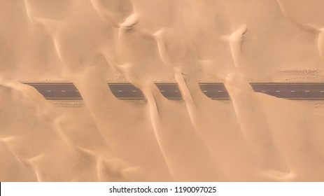 Aerial View Of A Desert Road Being Run Over By Sand Dunes Photographed From A Drone At Sunrise. Dubai, UAE.