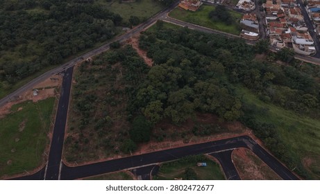 Aerial view of a developing suburban area with new roads bordering a dense forest and existing houses