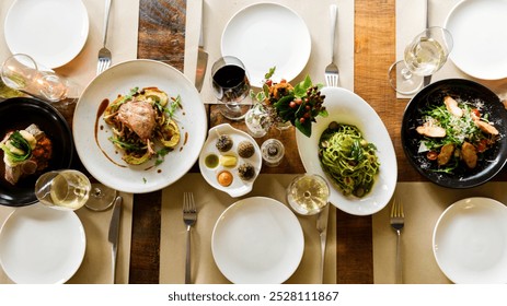 Aerial view of a dining table set with plates of pasta, salad, and meat dishes. Elegant food course with wine. The dining experience. Top view of dinning table set. Long served restaurant table