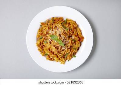 Aerial view of a dinner dish full of tomato and basil fusilli pasta on a pastel grey background