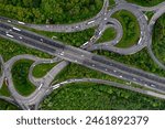 Aerial view directly above a busy M62 UK motorway intersection with roundabout and overbridge cutting through green woodland in an environmental disaster image