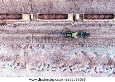 Aerial view directly above a mineral ore quarry with loaded railway wagons and a tractor with water bowser spraying water to dampen down airborne dust