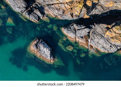 Aerial View Directly Above Rugged Rocky Outcrop Of Land Jutting Into A, Emerald Green Ocean With Sand Sea Bed In Cornwall, UK With Copy Space