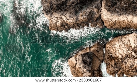 Aerial view directly above white waves breaking on harsh stone rocks in a rugged environment on the Cornwall coast with copy space above emerald green ocean