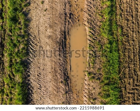 Aerial view of a dirty dirt road with mud, grass and tracks between fields and fields in autumn