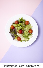 Aerial view of a dish full of classic garden salad on a pastel pink and purple background
