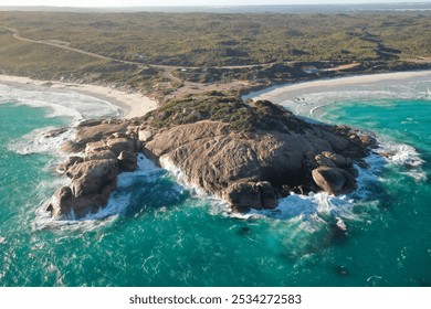 Aerial view of a dramatic coastal rock formation surrounded by turquoise waters, with lush greenery in the background and waves crashing against the rocks. The natural beauty of a pristine beach scene - Powered by Shutterstock