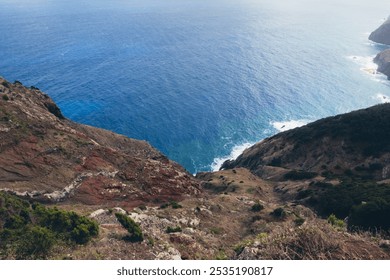 Aerial view of a dramatic coastline with a deep blue ocean crashing against the rocks.  The rugged cliffs and lush green vegetation provide a picturesque backdrop to this stunning natural landscape.