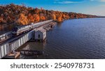 An aerial view of a drawbridge on the Hudson River in upstate, NY. Taken on a sunny day in autumn where the calm, reflective waters are surrounded by colorful trees with the changing fall foliage.