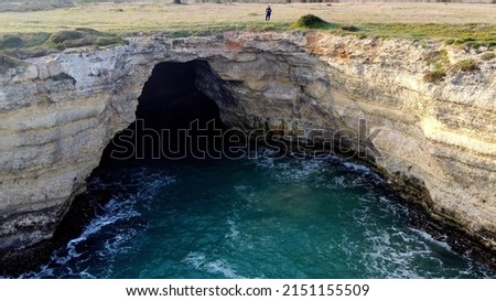 Aerial view from a drone flying over an amazing rock face that descends vertically to the sea and shows a sea cave with a huge opening