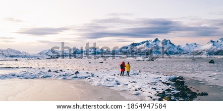 Aerial view from drone of male and female photographers in expedition walking on frozen shore of lake in Scandinavia, wanderlust couple of bloggers with cameras taking photo of scenery winter nature