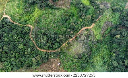 Aerial view from drone of mountain road with sun shining in forest. Top view of a road on a hill in a beautiful lush green forest in Thailand. Natural landscape background.