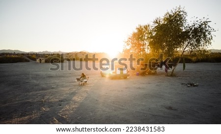 Aerial view drone shot of woman doing van life living and working in remote area of nevada usa desert with sun setting in distance with warm orange hues and bright over exposed sky for copy space.