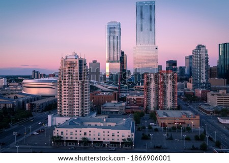 An aerial view of dusk settling over downtown Edmonton in the summer. There is a pinkish hue in the background and the glass skyscrapers are reflecting the light.