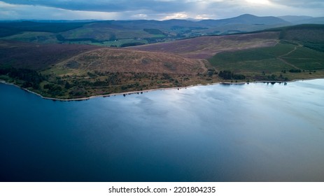 Aerial View At Dusk Of A Water Reservoir, Green Meadows, And Distant Mountains