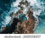 Aerial view early morning light with ocean waves flowing over rocks around North Curl Curl ocean rock pool during storm.