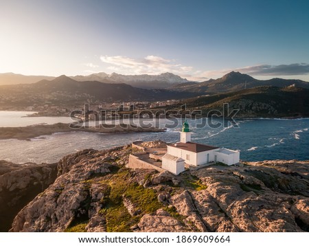 Aerial view of early morning sun on the lighthouse at La Pietra in Ile Rousse in the Balagne region of Corsica with snow capped mountains in the distance