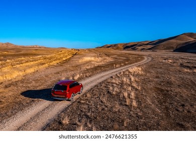 Aerial view of ed SUV driving on a dirt road in a desolate landscape in Gareji area in Georgia. The road winds its way through the dry, brown landscape, which is dotted with sparse vegetation. - Powered by Shutterstock