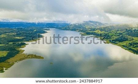 Aerial view of Embalse de Tominé in Guatavita, Cundinamarca. Showcasing serene water, lush greenery, and cloudy skies