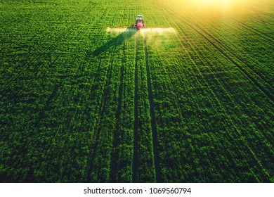 Aerial View Of Farming Tractor Plowing And Spraying On Field.