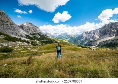 Aerial view of female hiker looking at Gardena Pass, Sass da Ciampac, Tor Bornech and Sass dla Luesa, Trentino Alto Adige, Italy. Alpine meadows and Passo Gardena.