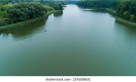 Aerial View Fisherman Is Fishing Sitting On An Inflatable Boat In Lake. Drone Wide Shot Adult Man Sailing On A Boat To Fish