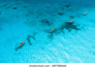 Aerial view of the fishing boats in clear blue water at sunny day in summer. Top view from above of boat, sandy beach. Indian ocean in Zanzibar, Africa. Landscape with canoe and clear sea. Travel