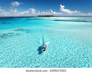 Aerial view of floating boat in clear azure water on summer day. Mnemba island, Zanzibar. Top view of yacht, sandbank in low tide, clear blue sea, sand, sky with clouds. Vacation, travel. Tropical