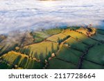 Aerial view of a fog filled valley surrounded by rural farmland in afternoon sunshine (Brecon Beacons, Wales, UK)