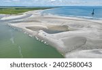 An aerial view of Folly Beach, North Carolina, on a summer day, showcasing the sandbar and lighthouse that make up the coastal landscape