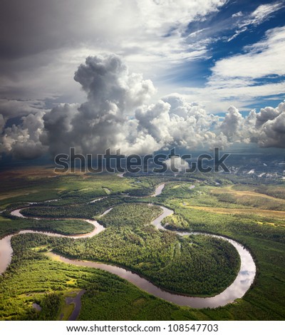 Aerial view of forest the river during summer day on background of great white clouds.