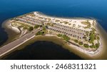 Aerial view of Fred Howard Park in Tarpon Springs, Florida, featuring parking lots, palm trees, sandy beaches, and surrounding blue waters under a clear sky.