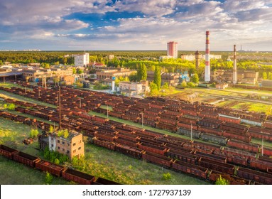 Aerial View Of Freight Trains. Railway Station With Wagons. Heavy Industry. Industrial Landscape With Train In Depot, Smoke Stack, Green Trees, Buildings, Blue Sky At Sunset. Top View. Transportation 