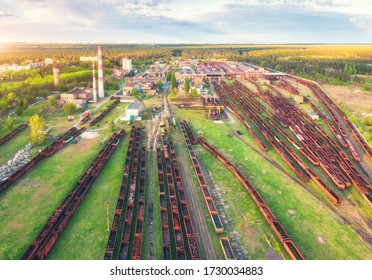 Aerial View Of Freight Trains. Railway Station With Wagons. Heavy Industry. Industrial Landscape With Train In Depot, Smoke Stack, Green Trees And Grass, Buildings At Sunset. Top View. Transportation 