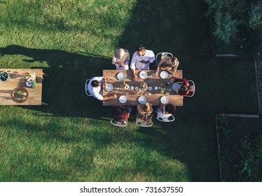 Aerial View Of Friends Enjoying Meal At Outdoor Party.  Group Of People Sitting Around A Table In Garden Restaurant And Having Meal Together.