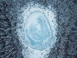 Aerial View Of Frozen Pond In The Middle Of Winter Forest.