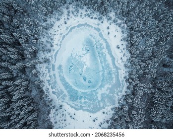 Aerial view of frozen pond in the middle of winter forest.