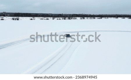 Aerial view of a frozen snow and ice covered lake with bending track. Clip. Drifting car on a winter day.