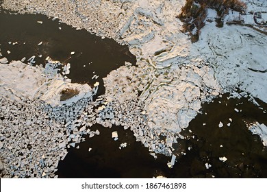 Aerial view of the frozen surface of the sea with ice floes and the coast with islands in the sunset light. Abstract winter landscape of a northern country like a map with drone.