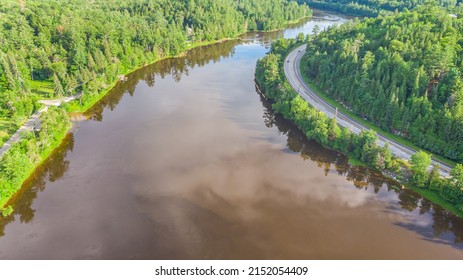 Aerial View of the Gatineau River near the village Wakefield, Canada. Clouds reflecting in the river water, a street with cars winds along the course of the river. Green lush Canadian forest landscape