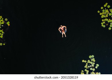 Aerial view of a girl in a swim ring, between Lily pads in pond water - overhead, drone shot